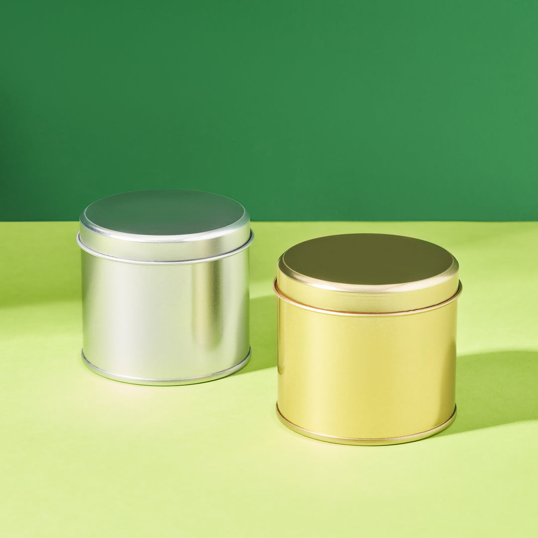 Tall round welded side seam tins in gold and silver on a green background. 
