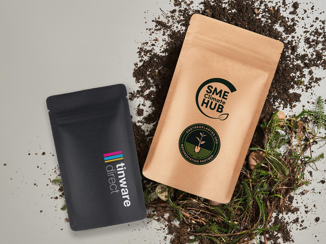 Printed compostable stand up pouch packaging in black and brown resting on soil with a white background